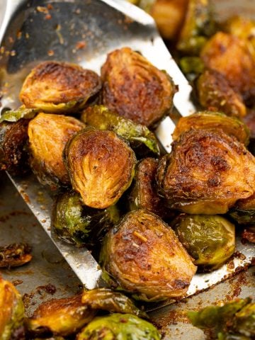 Oven roasted brussels sprouts showing a brown caramelization and picked up with a spatula.