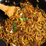 Top view showing yaki udon made in a black wok, with noodles coated in sauce and ground pork.