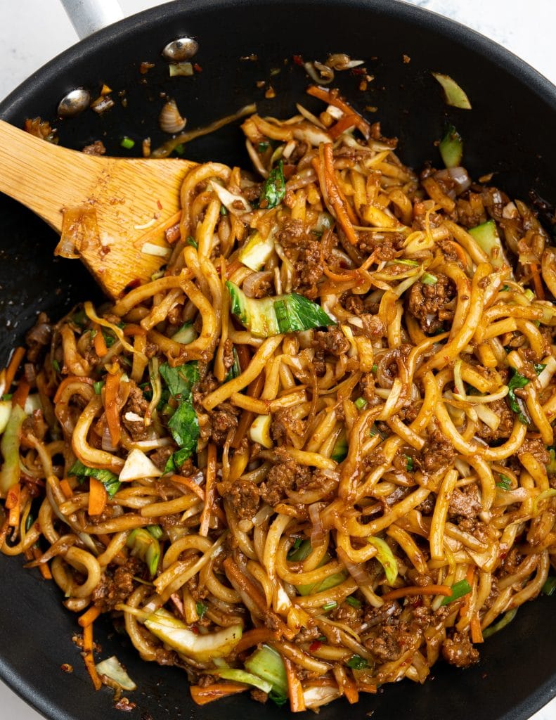 Top view showing yaki udon made in a black wok, with noodles coated in sauce and ground pork.