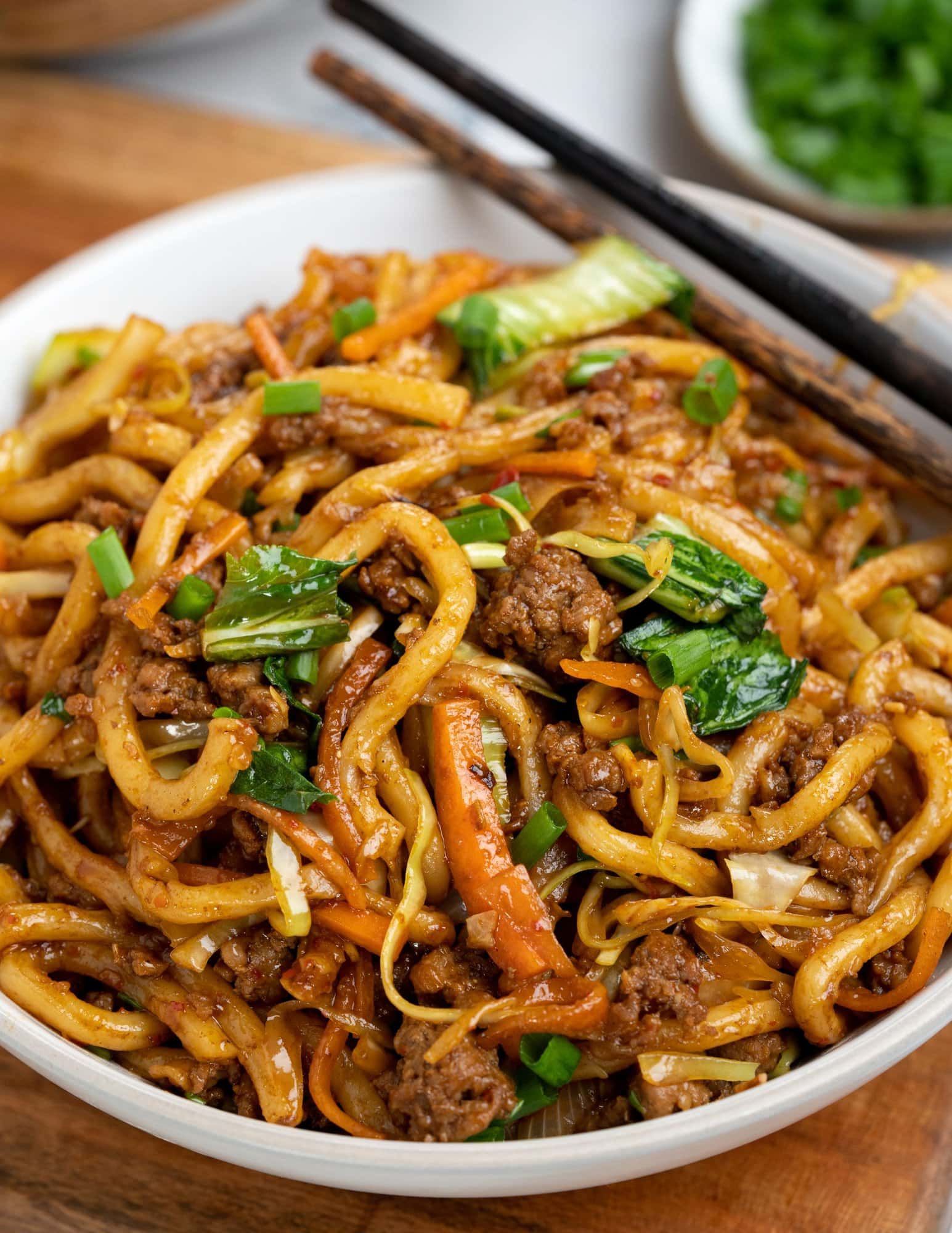 A white bowl serving of udon noodles stir fry made with ground pork, sliced veggies and savory soy-based sauce.