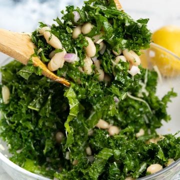 Picking up a portion of cannellini white beans salad with kale with a wooden spoon.