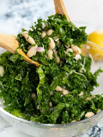 Picking up a portion of cannellini white beans salad with kale with a wooden spoon.
