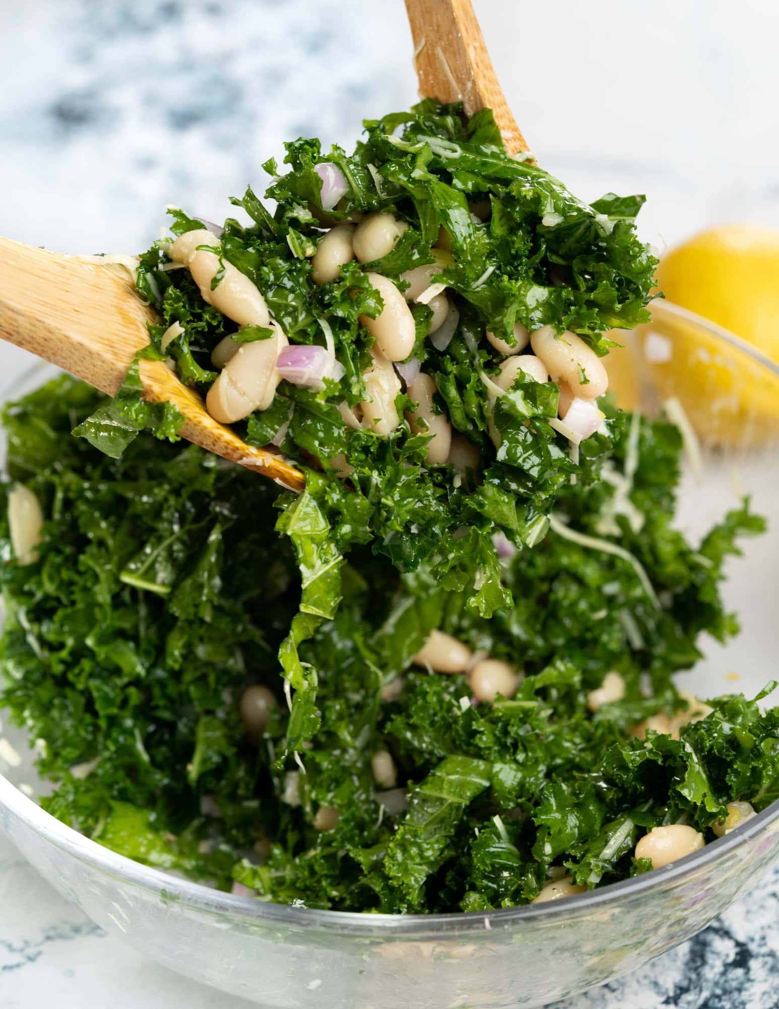 A bunch of white beans and kale salad being picked up with a wooden spatula.