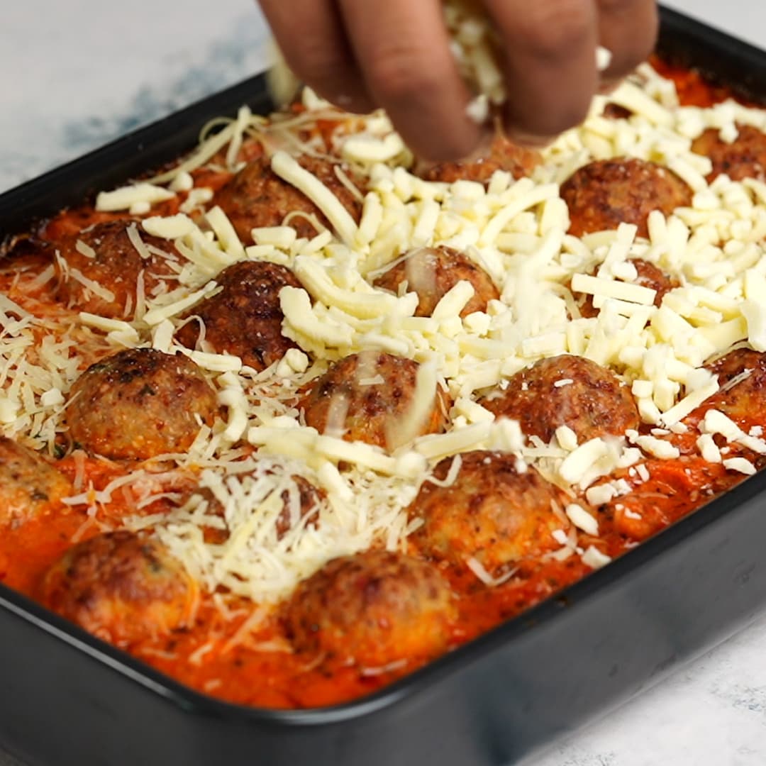 Cheese is spread evenly on the cooked meatball and pasta mixture before placing it in oven again for the cheese to melt.