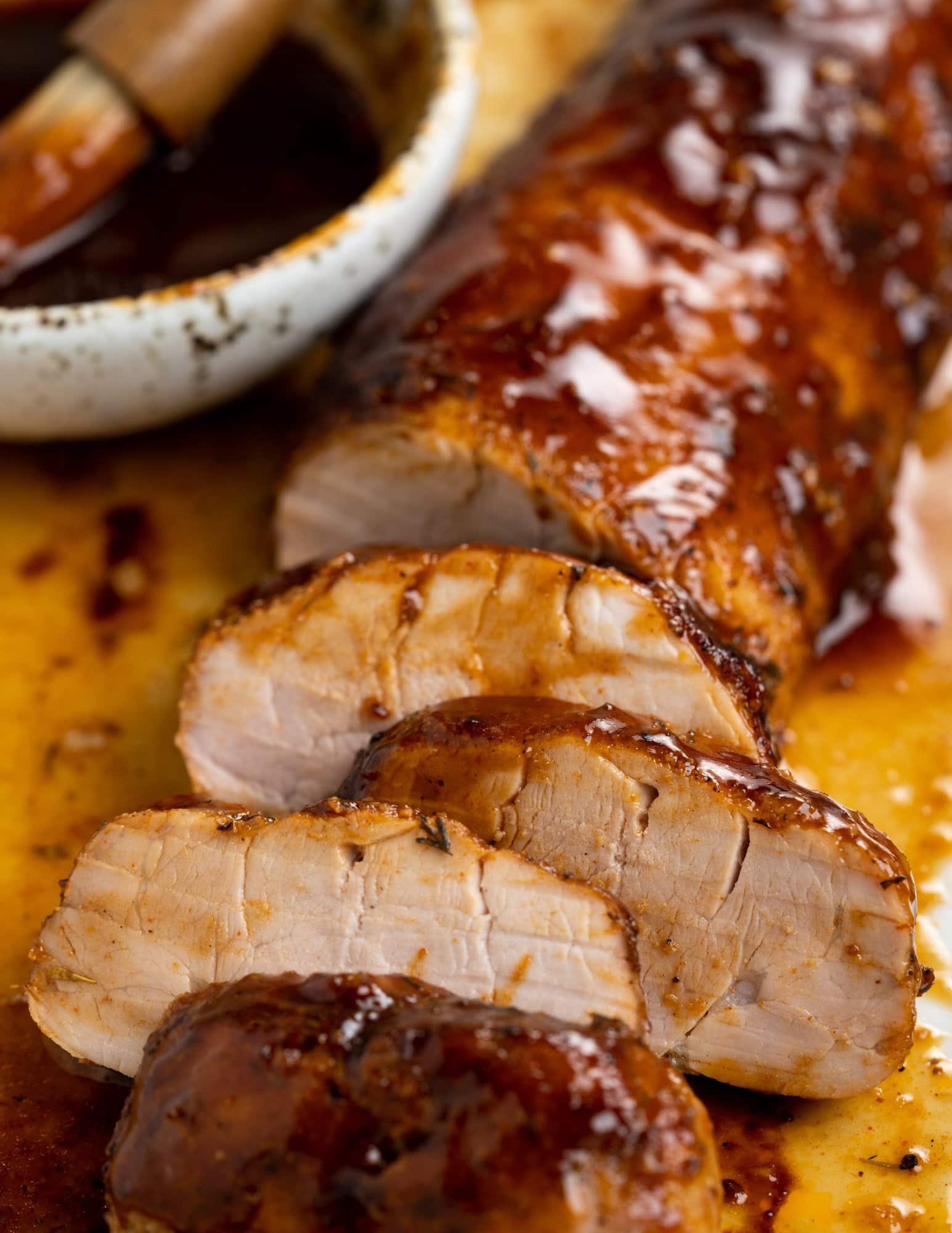 A shiny BBQ glaze on baked pork tenderloin and chopped cuts show light pink color.