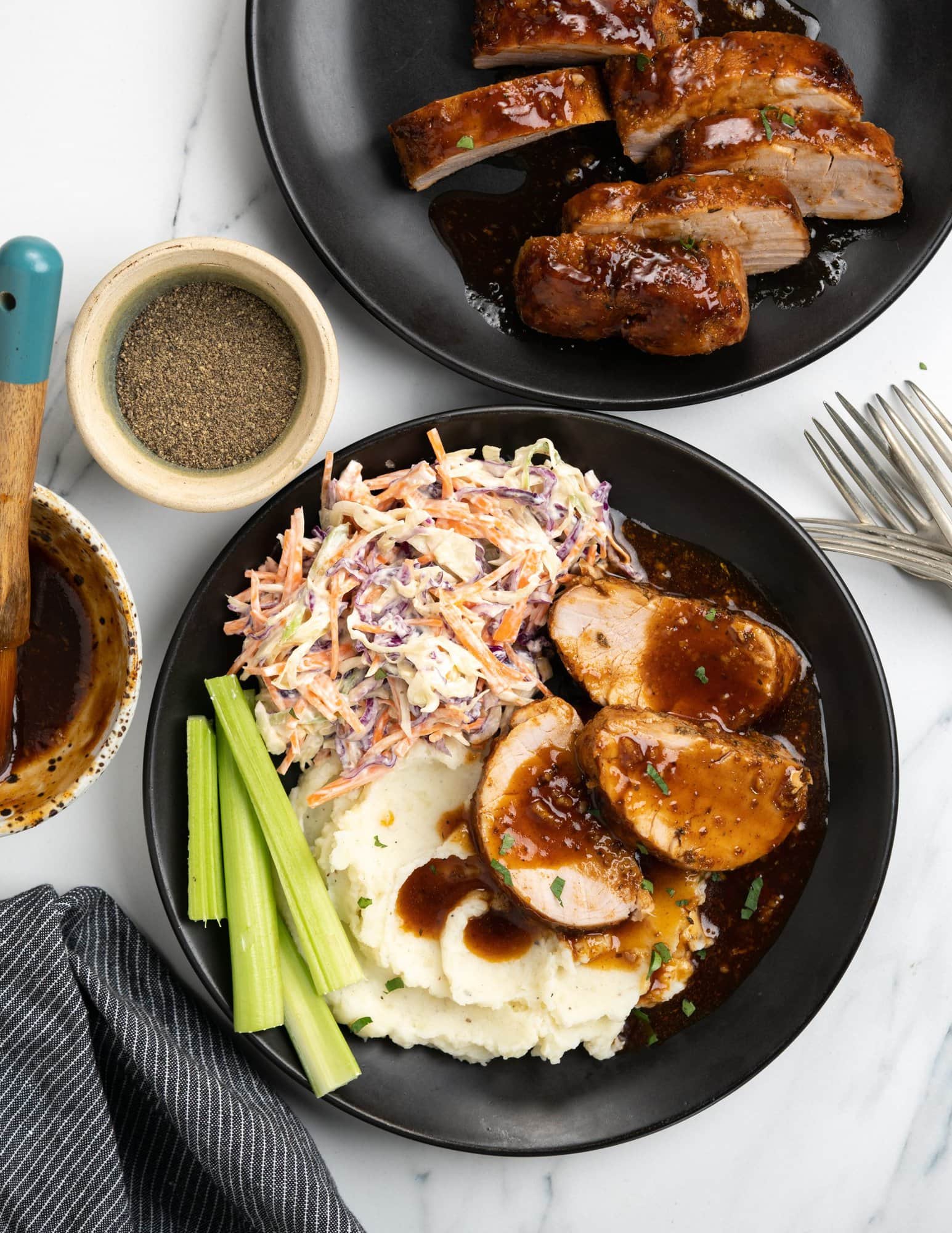 Baked pork tenderloin with a shiny BBQ glaze, served with mashed potatoes and coleslaw in a black plate.