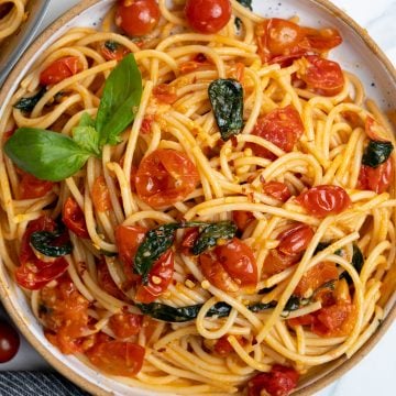 Spaghetti pasta is made with cooked cherry tomatoes, parsley and red pepper flakes and topped with fresh basil.