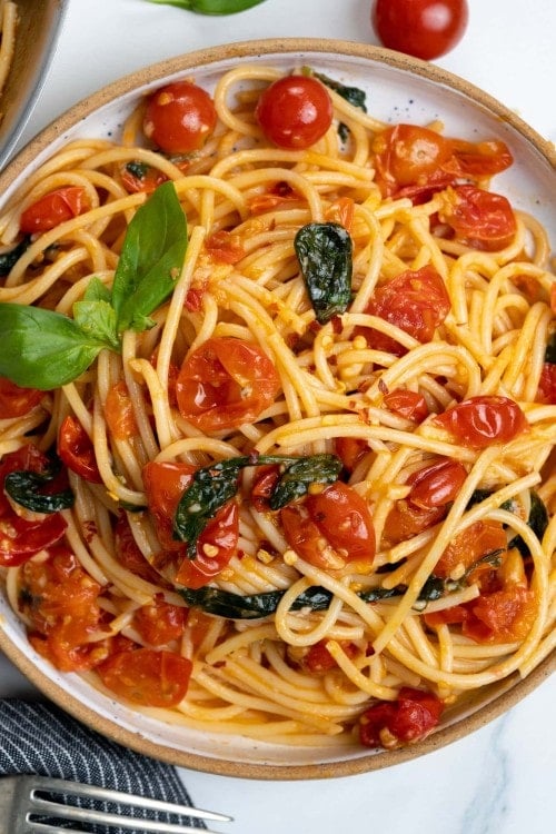 Spaghetti pasta is made with cooked cherry tomatoes, parsley and red pepper flakes and topped with fresh basil.