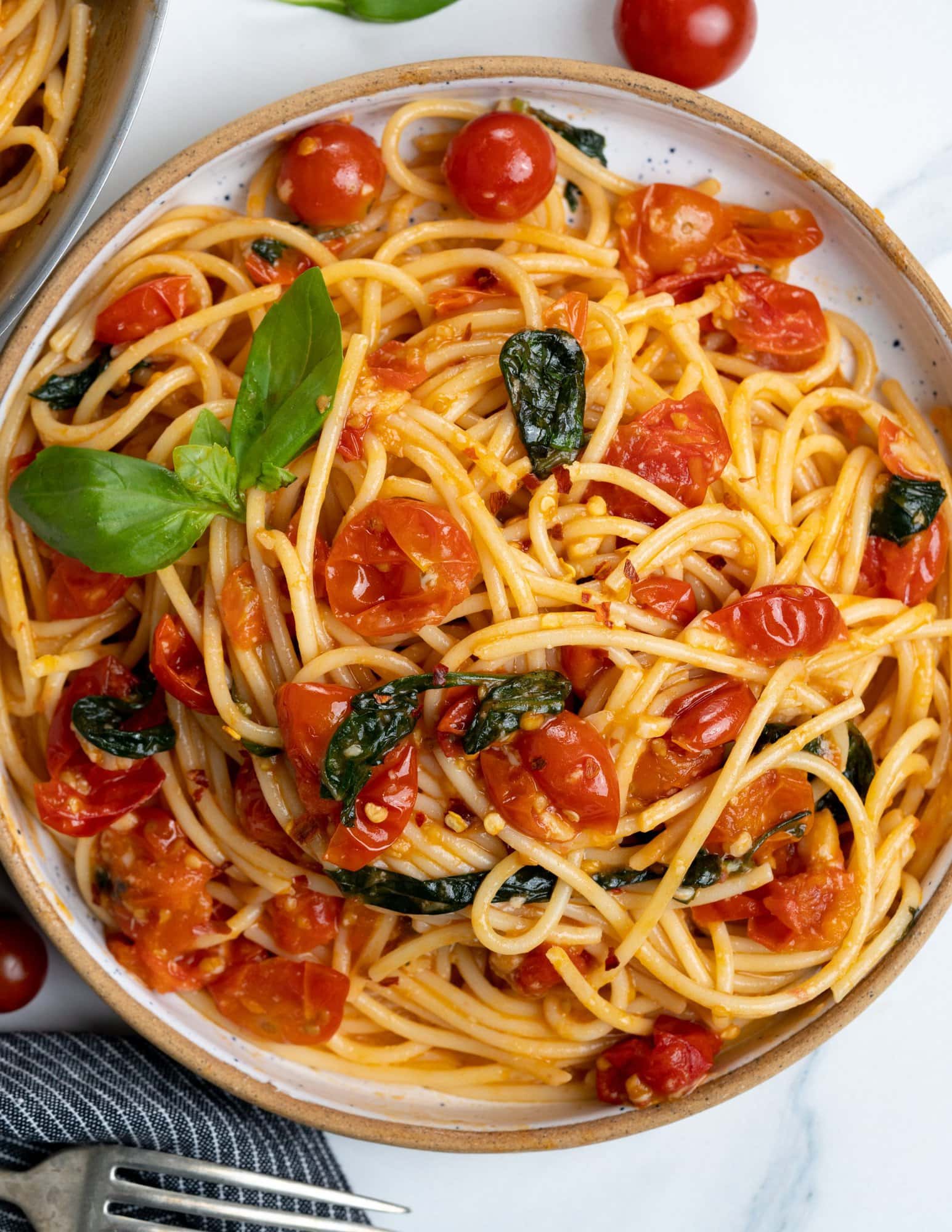 Spaghetti pasta is made with cooked cherry tomatoes, parsley and red pepper flakes and topped with fresh basil