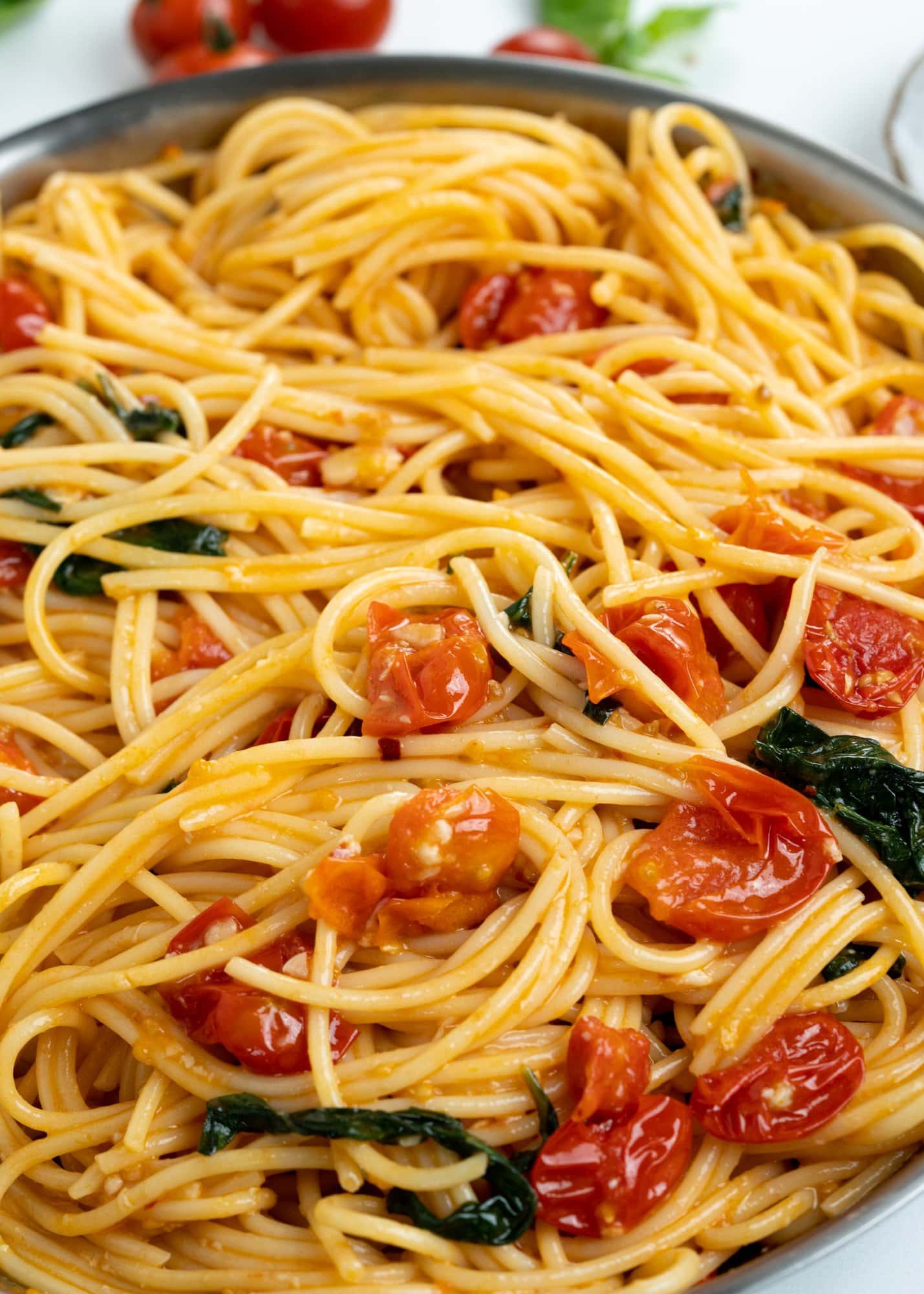Close up of tomato pasta shows spaghetti, crushed cherry tomatoes and parsley.