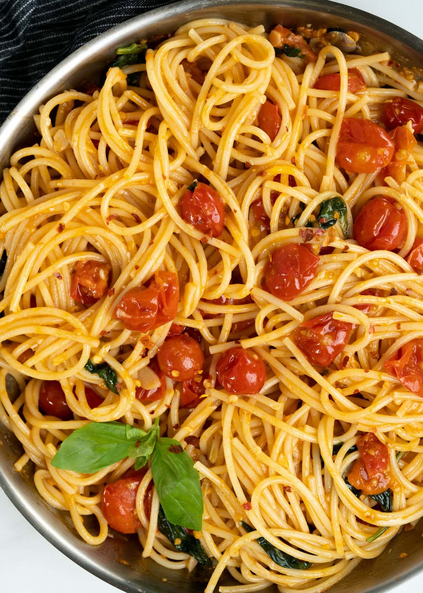 Top view of spaghetti tomato pasta shows spaghetti tossed in a sauce of cherry tomatoes, garlic and red pepper flakes and topped with fresh basil.