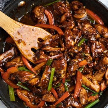 Chicken cooked in Chinese sauce with flavors from garlic in a black skillet and tossed with a wooden spatula