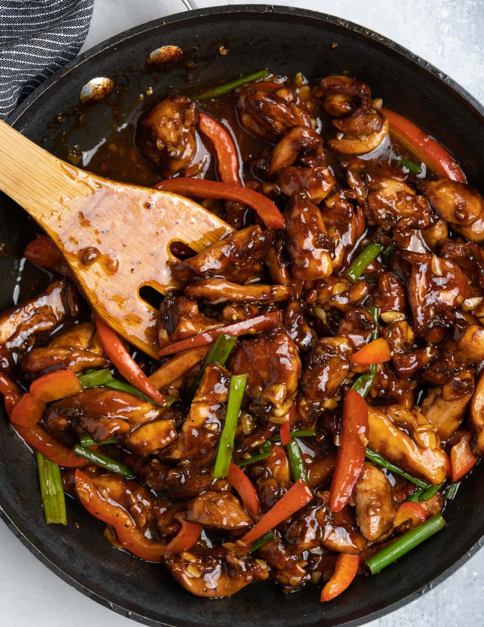 Chicken cooked in Chinese sauce with flavors from garlic in a black skillet and tossed with a wooden spatula