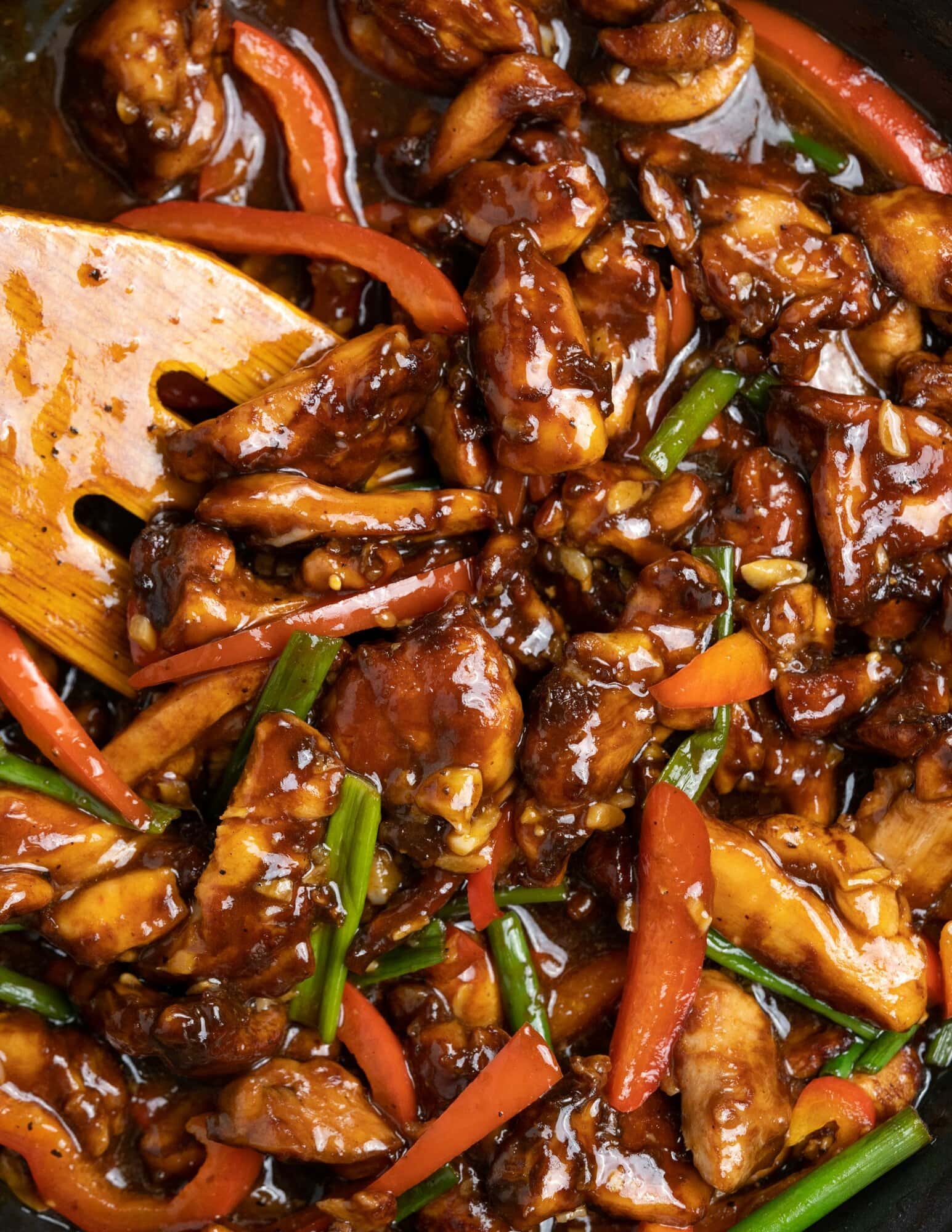 A close-up view of Chinese garlic chicken shows chicken and sliced bell pepper coated with a dark soy-based sauce with flavor intensified by garlic