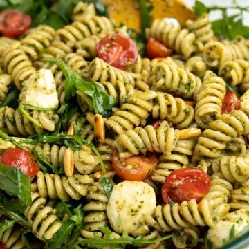 close view of pesto pasta salad shows vibrant colors of green pesto and rocket leaves, cherry red tomatoes, cheese