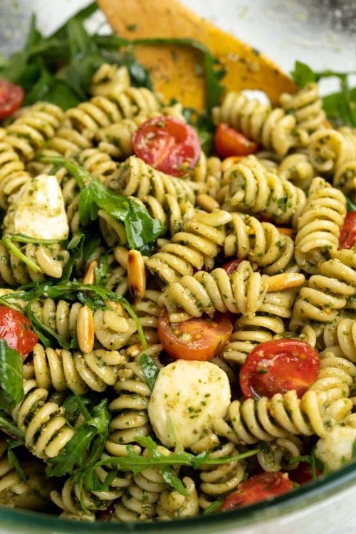 close view of pesto pasta salad shows vibrant colors of green pesto and rocket leaves, cherry red tomatoes, cheese