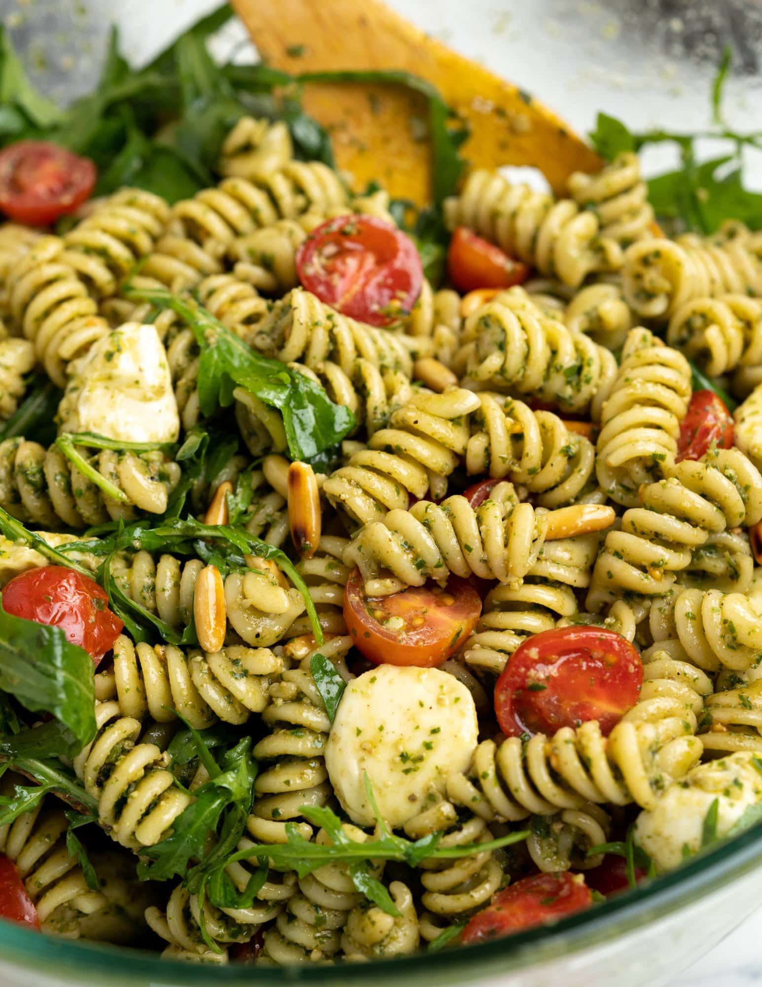 Close view of fusilli tossed in a pesto sauce and other ingredients to make a vibrant and fresh summer pesto pasta salad.