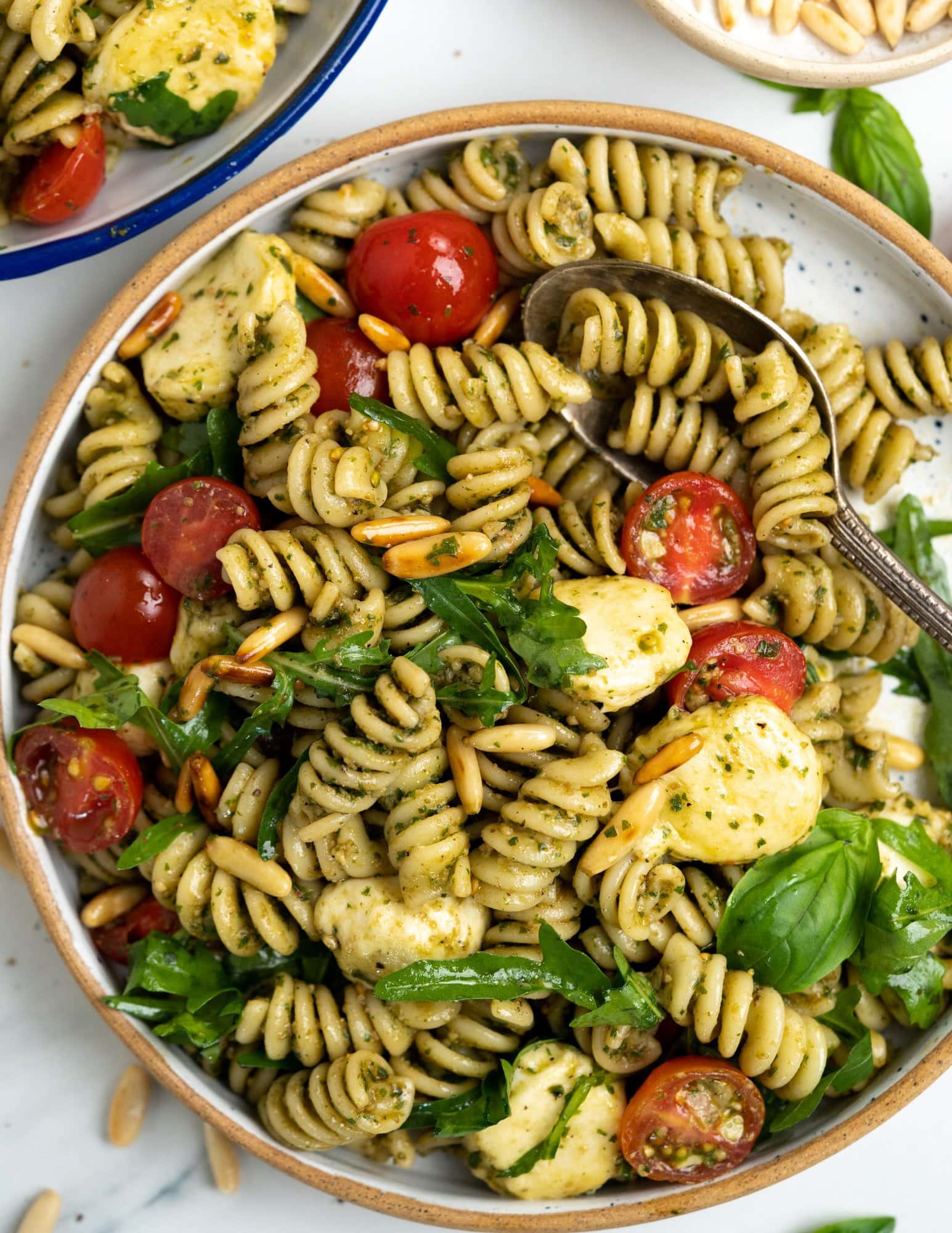 Fresh and vibrant colors of pesto pasta salad served in a plate.
