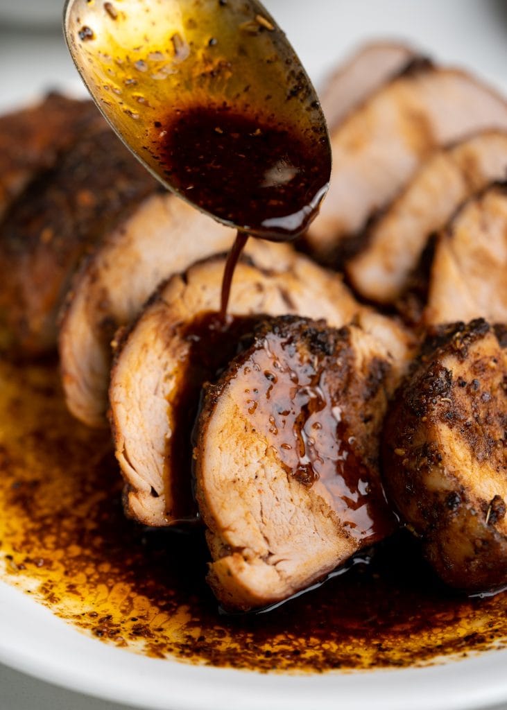 Saucy drippings from oven baked pork tenderloin spooned over a horizontal stack of slices.