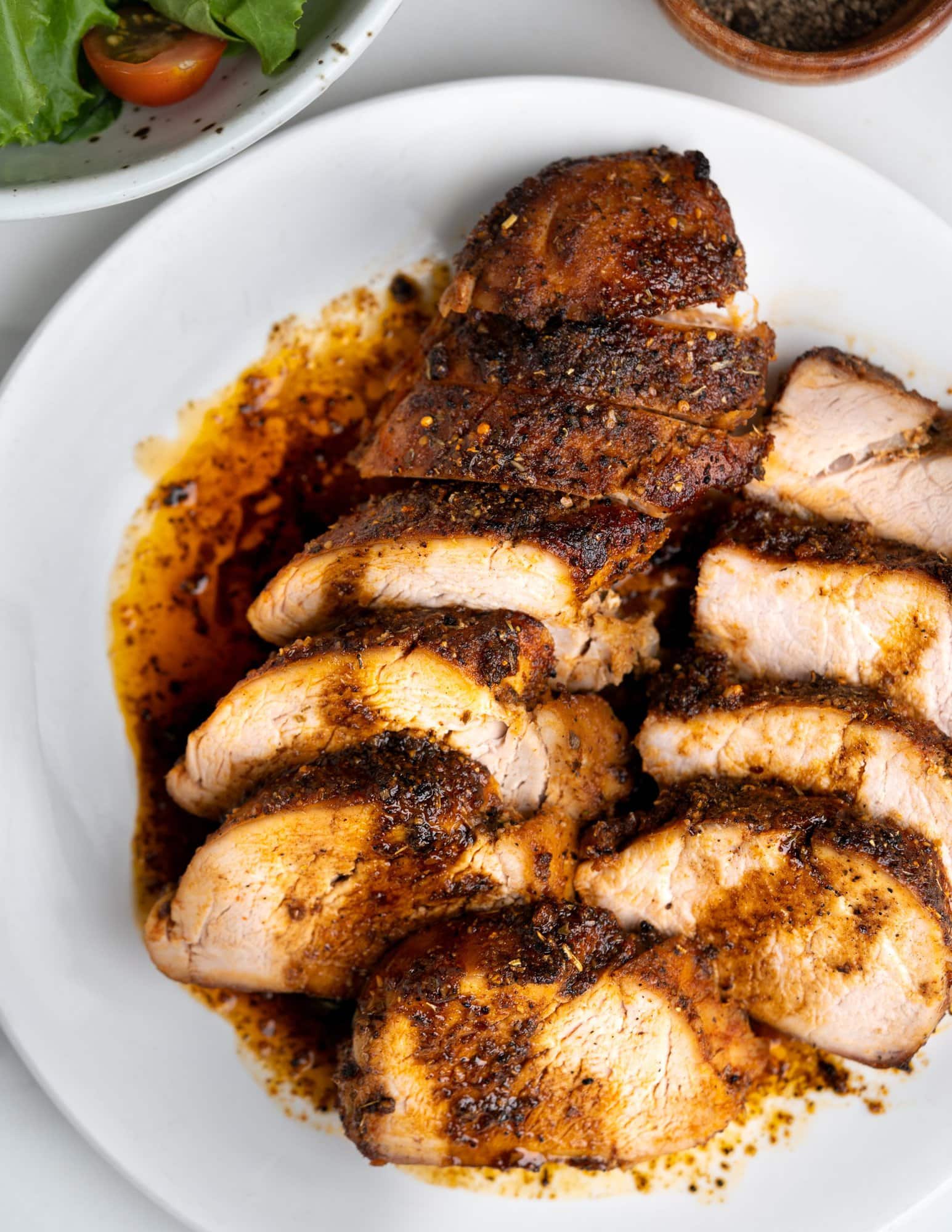 Roasted pork tenderloin in oven and slices stacked horizontally in a white plate shows a great crust and flavorful saucy drippings.