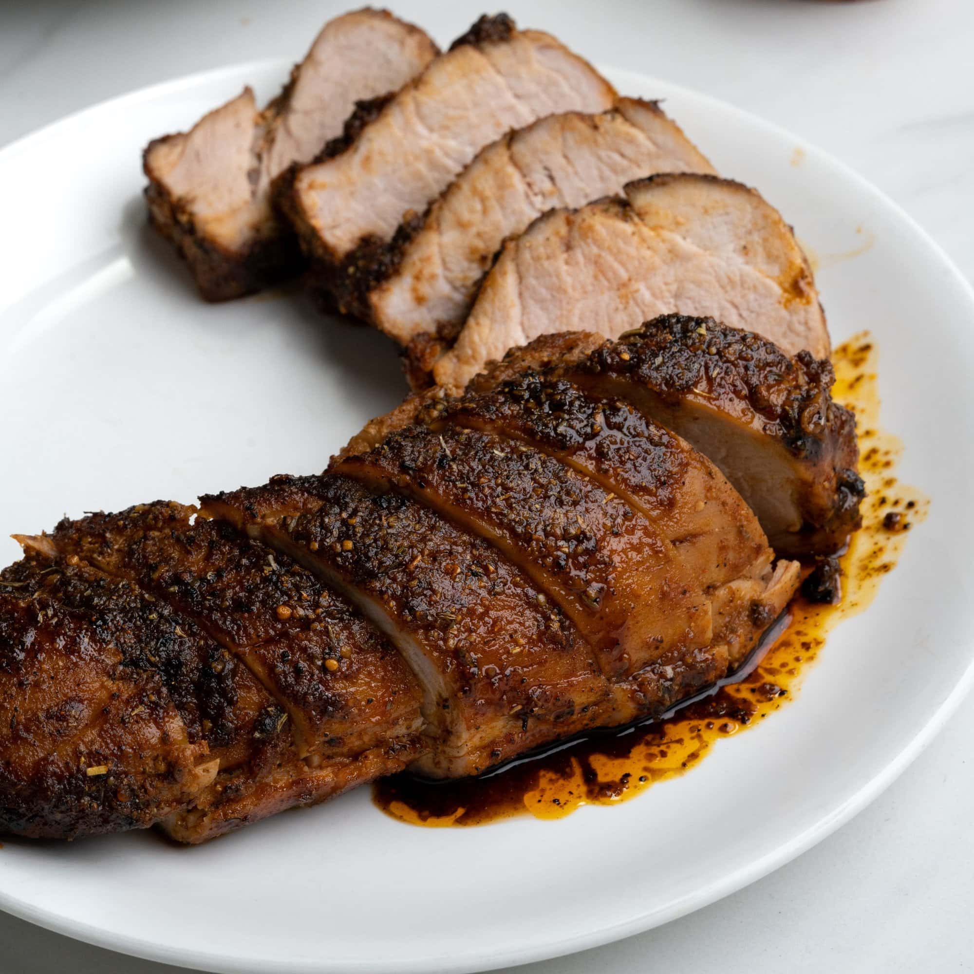 Pork tenderloin roasted in oven and the slices are arranged in a white plate. Few show a great crust and others the tender cooked meat.