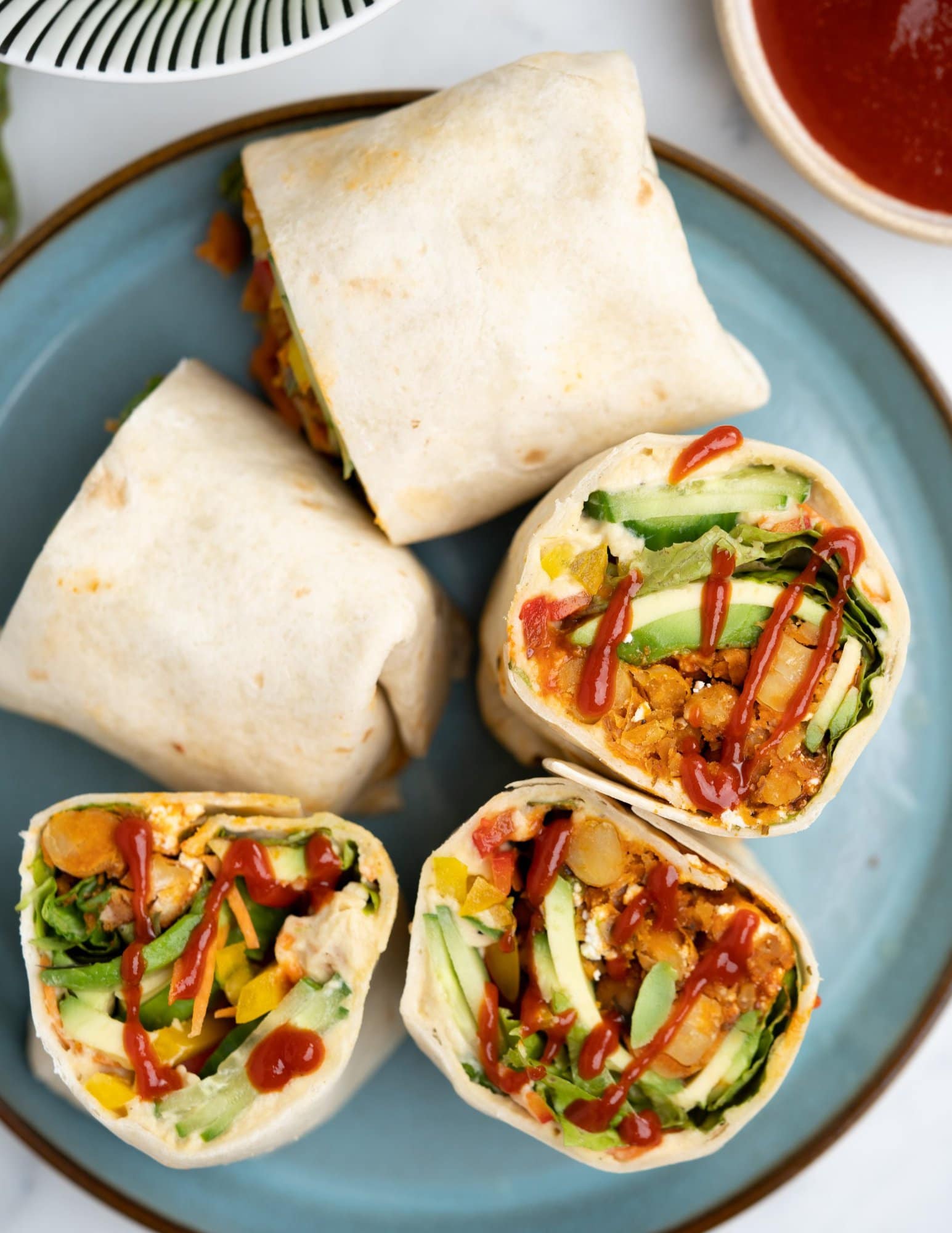 Tortilla wrap has a layer of creamy hummus , then topped with lettuce, cucumber, carrots, bell pepper, spicy chickpeas , hot sauce and feta. 