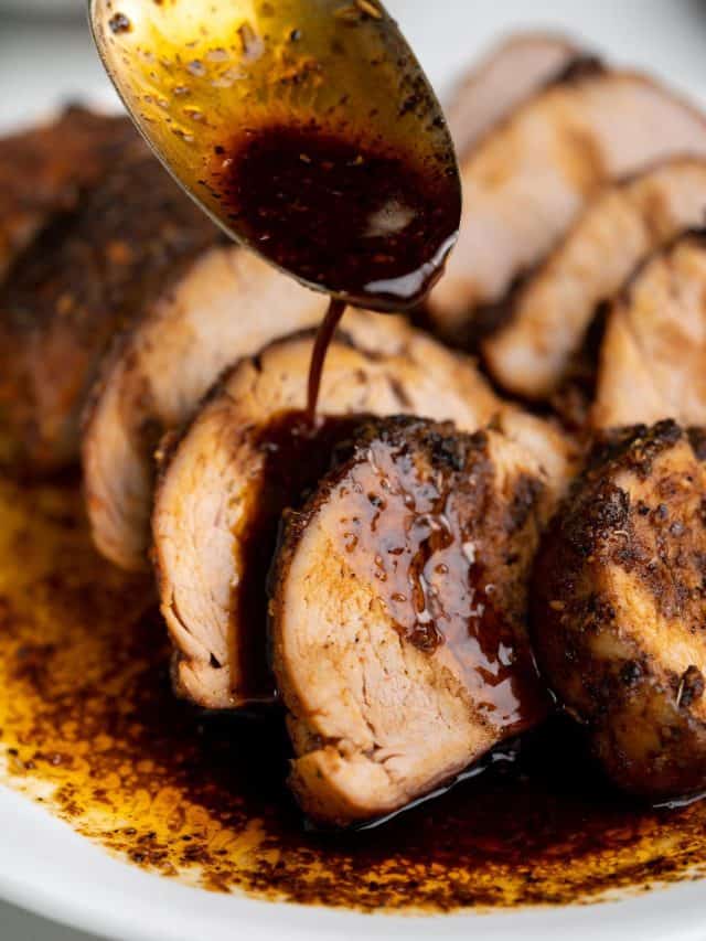 Saucy drippings from oven baked pork tenderloin spooned over a horizontal stack of slices.