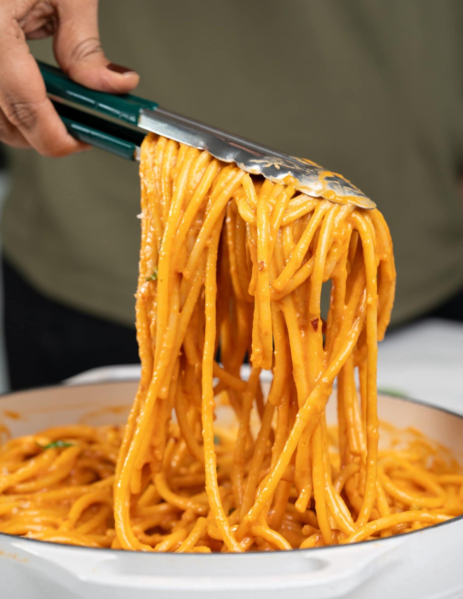 Picking bucatini coated with a creamy tomato and roasted red bell pepper sauce with a spatula.