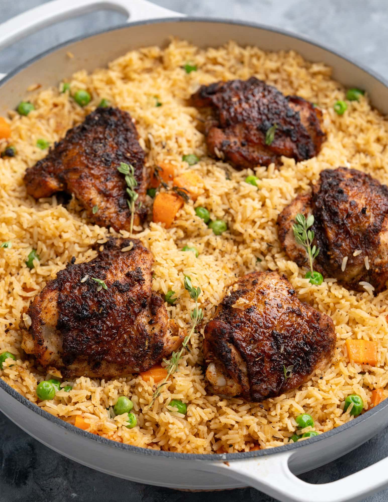 Image shows crispy chicken thighs, flavored rice , cooked carrots and peas, baked in a Dutch oven