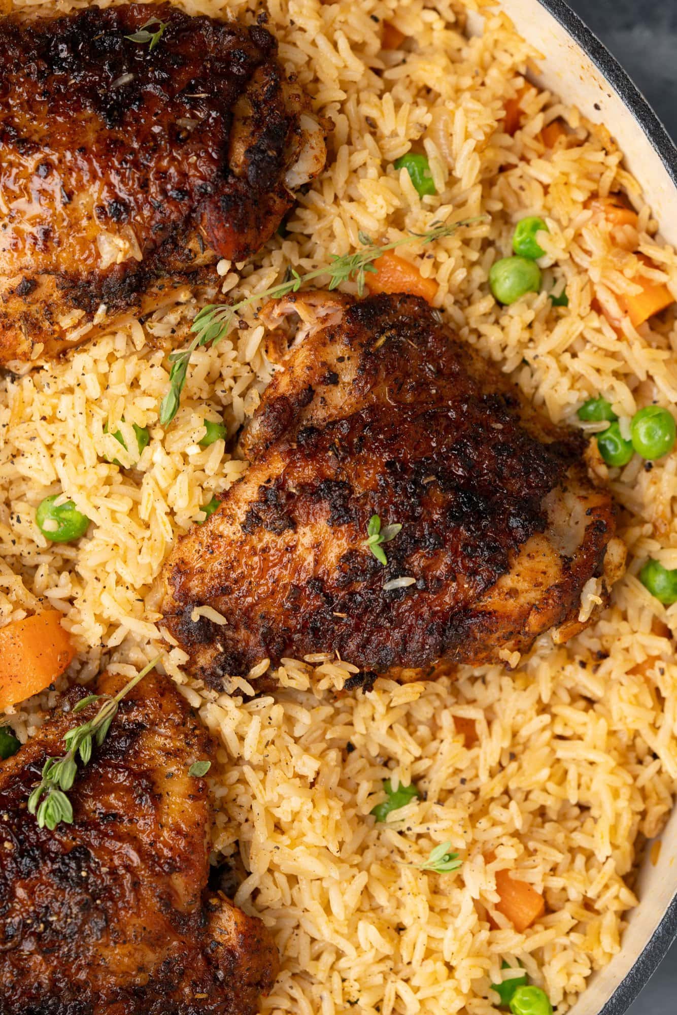 Image shows crispy chicken thigh baked along with flavored rice, with green peas and carrots.
