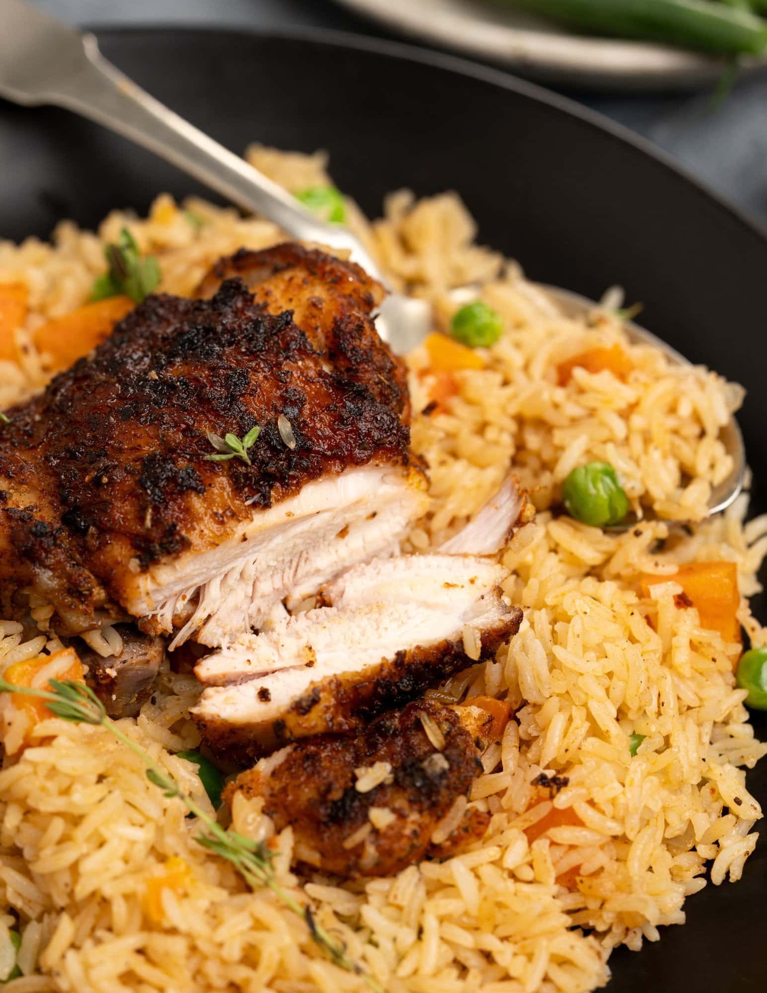 Close up image shows tender chicken cut from a crisp top thigh that was baked with rice.