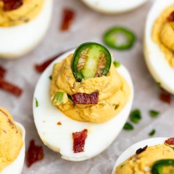 A single jalapeno deviled egg with jalapeno slices and bacon bits as garnish on top of creamy stuffing.