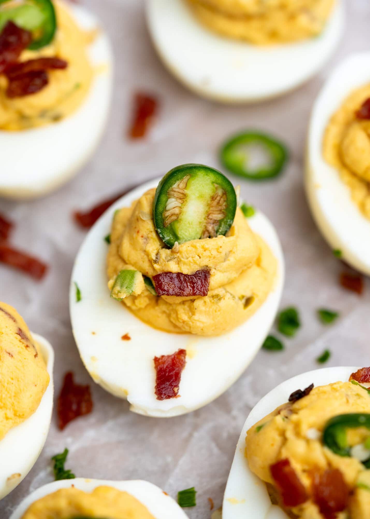 Close up view of a deviled egg with yolk, mayo and cheese stuffing and garnished with jalapeno's and bacon bits.