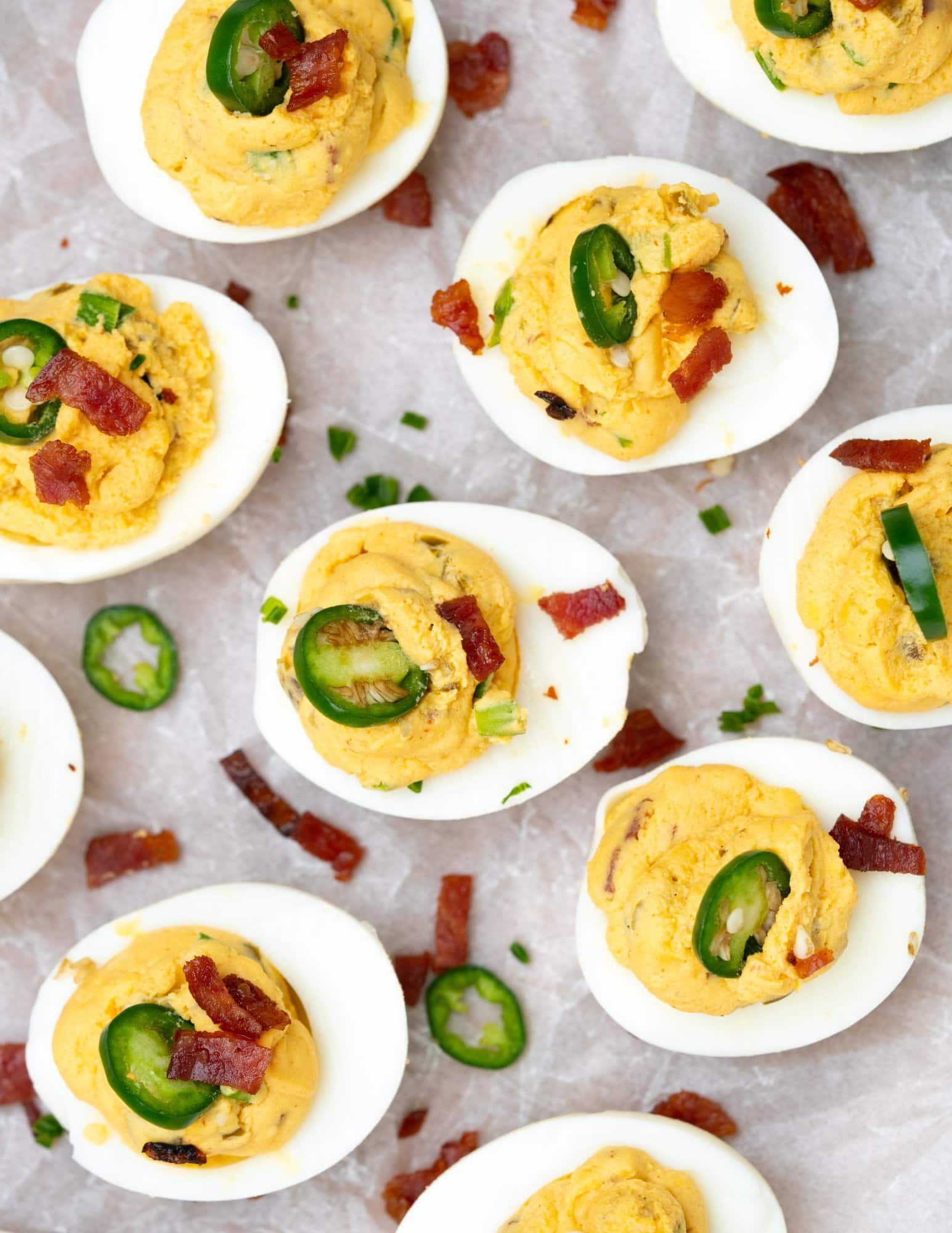 Many Deviled eggs presented with a creamy and soft yolk stuffing filled in and garnished with jalapeno slices and bacon bits.