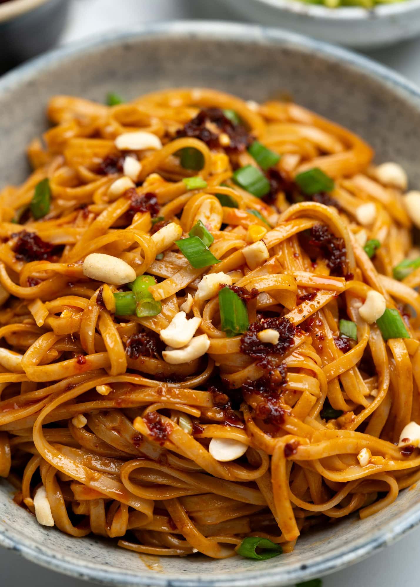 A bowl of creamy peanut butter noodles topped with chili crisp, salted peanut and green onion.