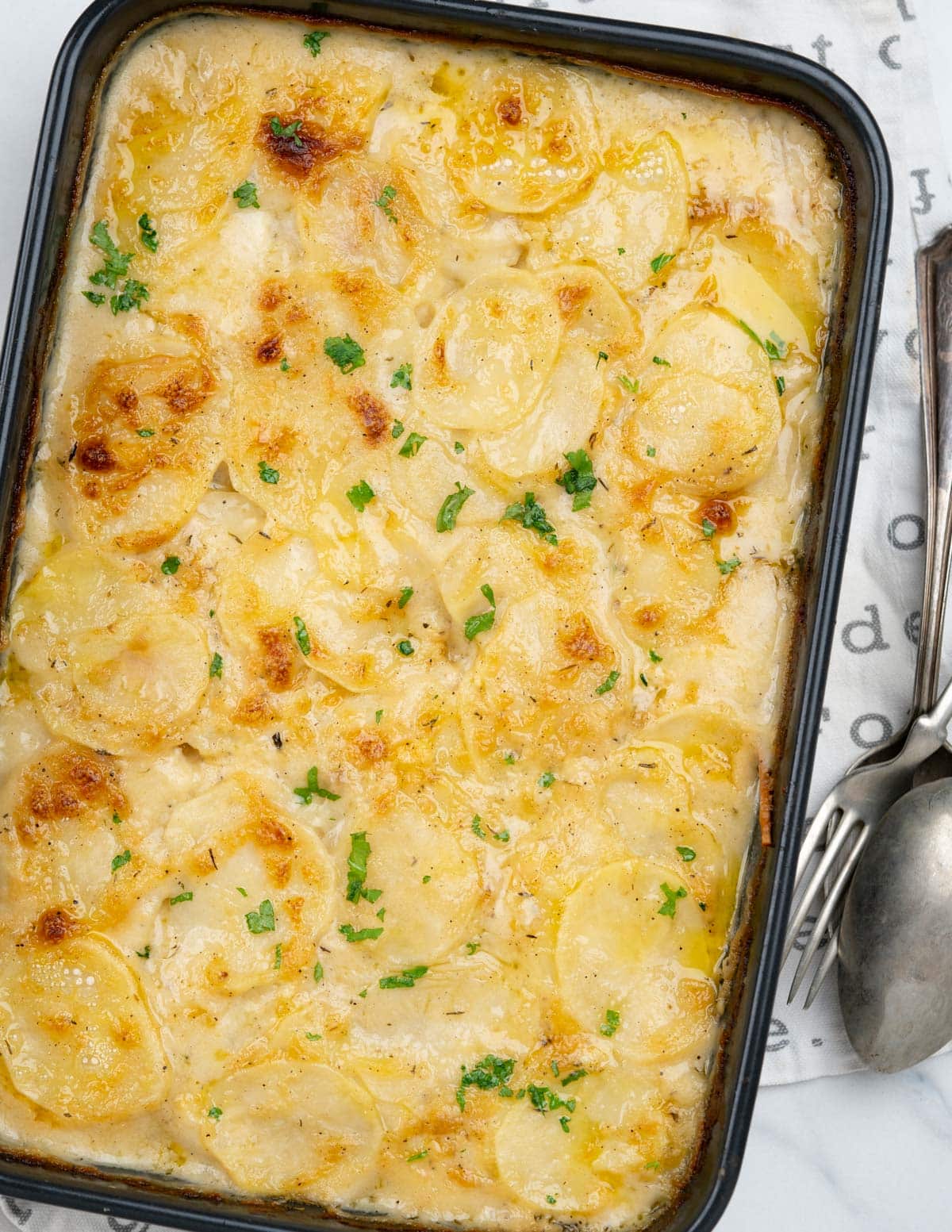 Cheesy sauce and potatoes get a light golden crust on top from baking.It is sprinkled with chopped parsley.
