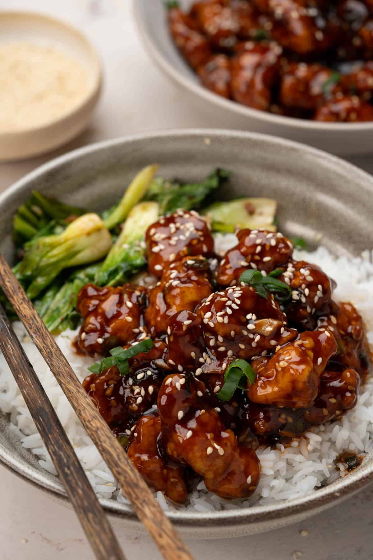 Sesame chicken served over a bowl of rice. Sesame seeds and chopped green onion sprinkled on top. 