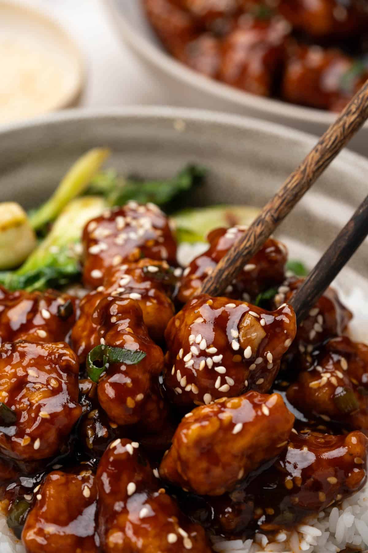 Sesame chicken served over a bowl of rice. Sesame seeds and chopped green onion sprinkled on top. 