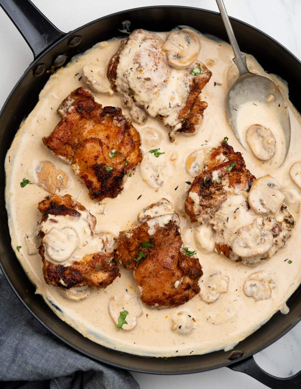 Skillet with crispy pan fried chicken thighs in a creamy mushroom sauce. 