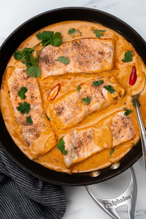 Four salmon fillets engulfed with a rich creamy coconut curry sauce, made in a black skillet