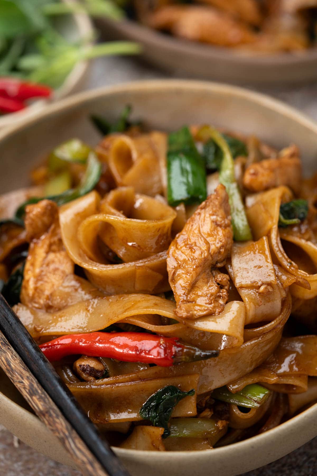 Close up view of Spice Drunken Noodles ( Pad Kee Mao) with juicy chicken, birds eye chilies and Thai basil.
