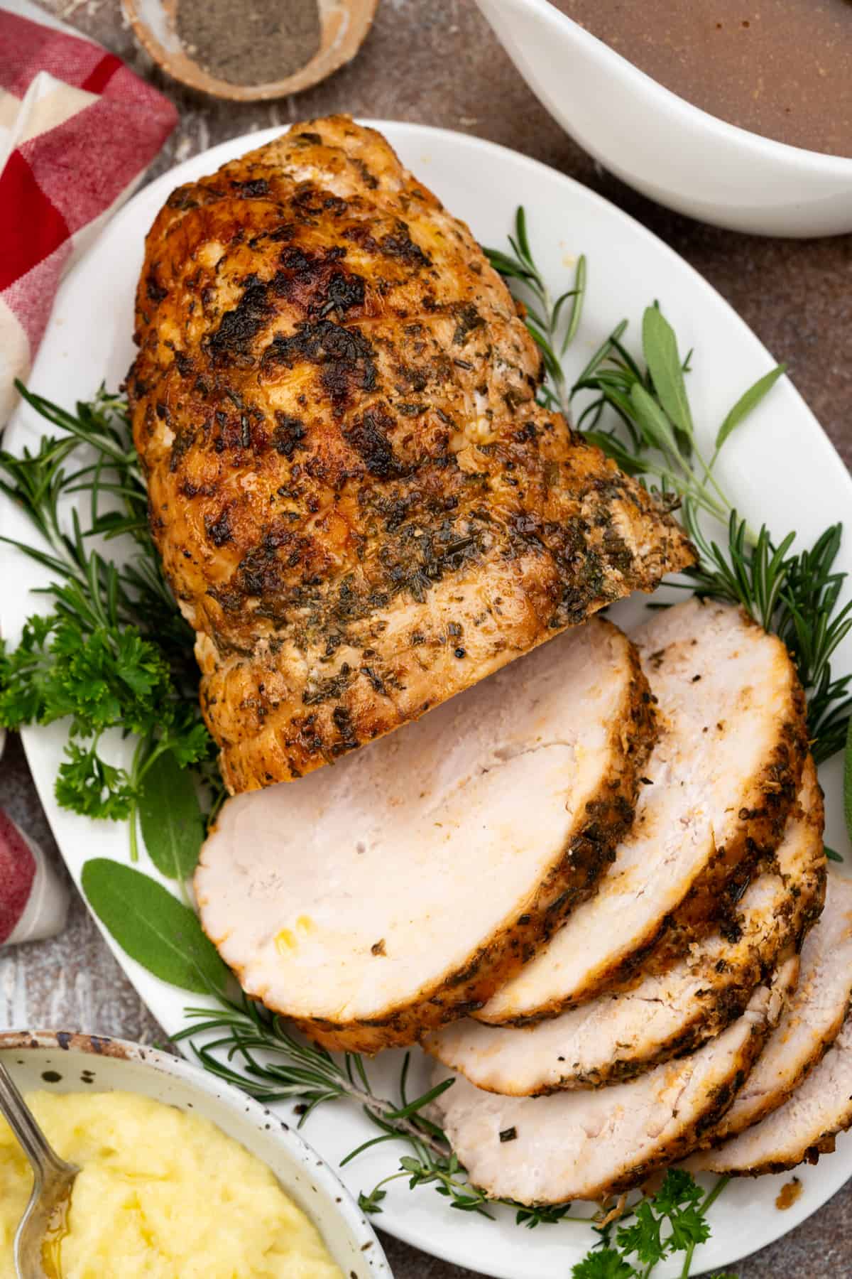 Shows half of a roasted turkey breast along with the other half sliced and plated on a bed of herbs.