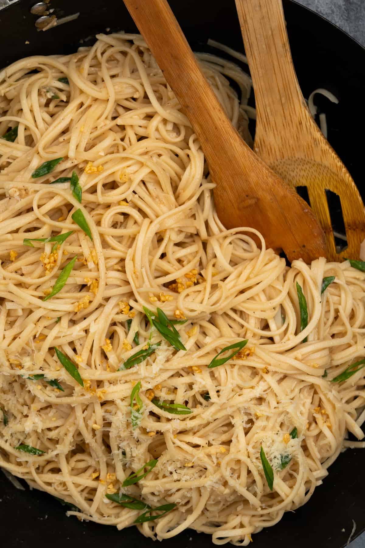 Bowl of buttery garlic noodles with grated parmesan cheese, sliced green onion and crispy garlic.
