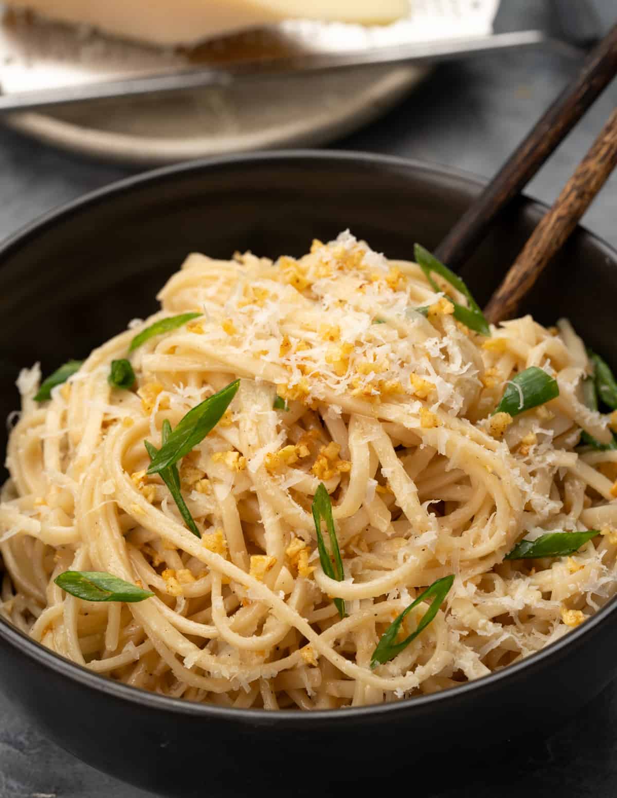 Bowl of buttery garlic noodles with grated parmesan cheese, sliced green onion and crispy garlic.