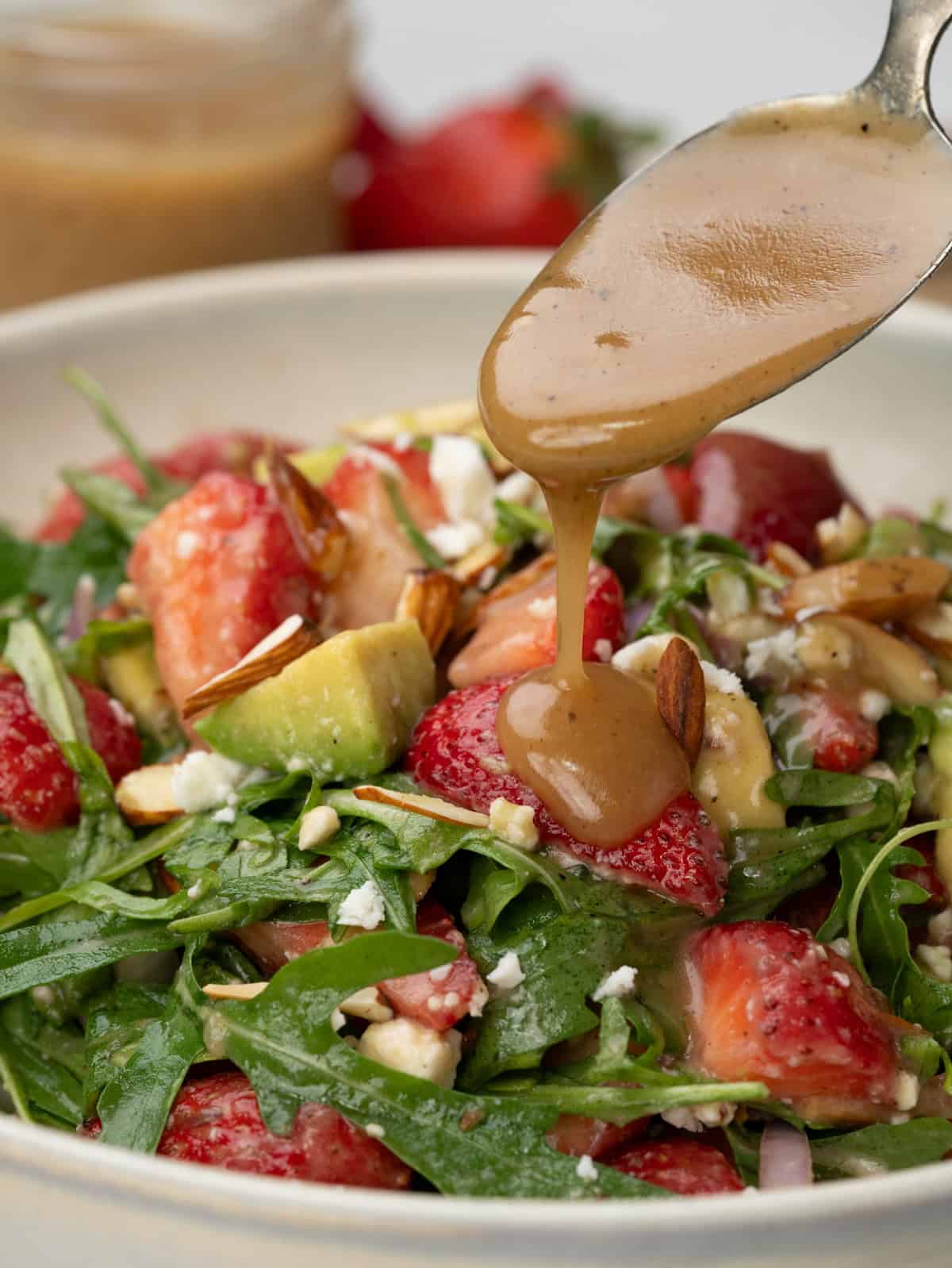 Creamy maple-Dijon dressing being poured over Strawberry Salad.