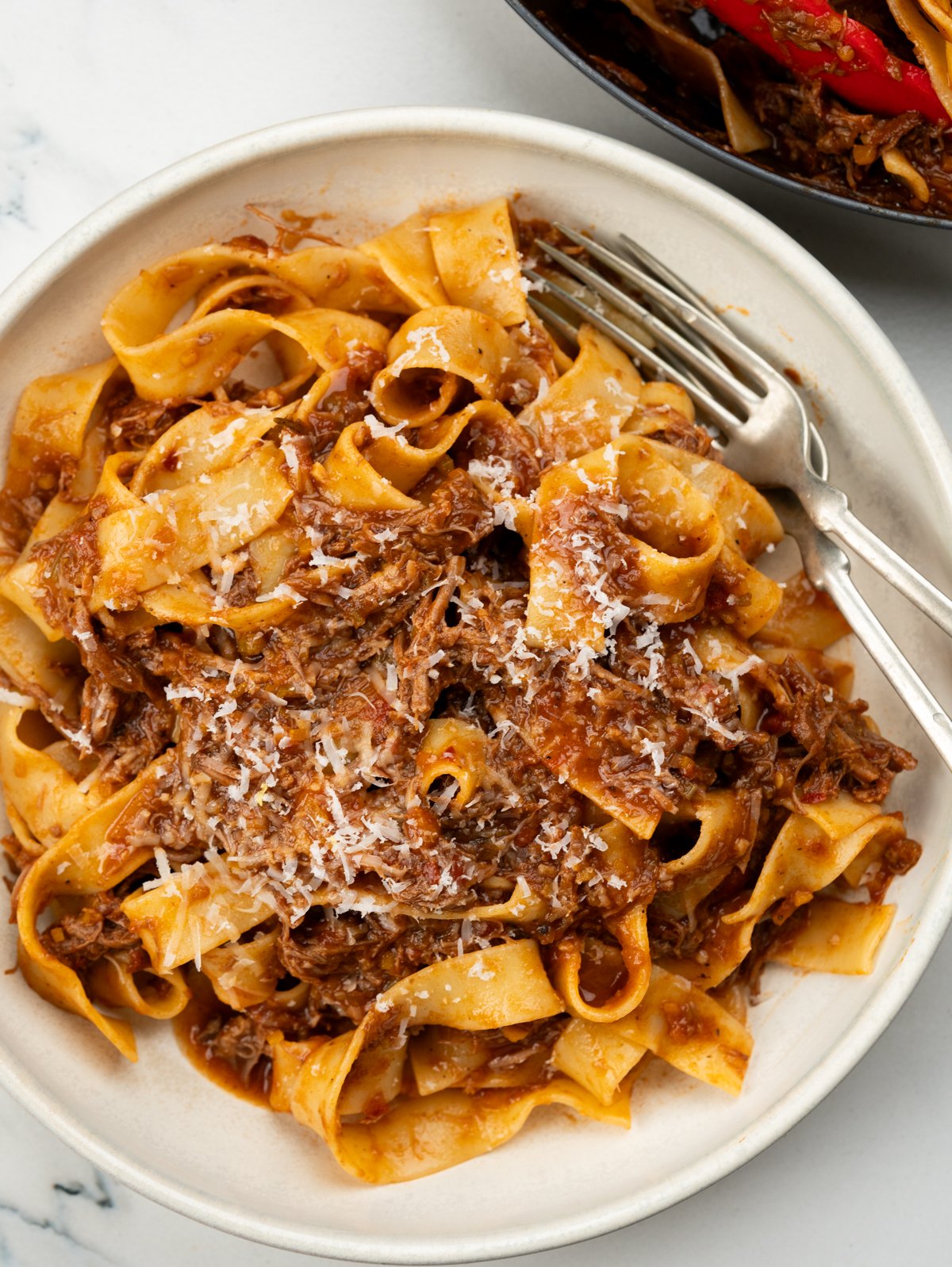 Braised lamb ragu with pappardelle pasta, garnished with parmesan.