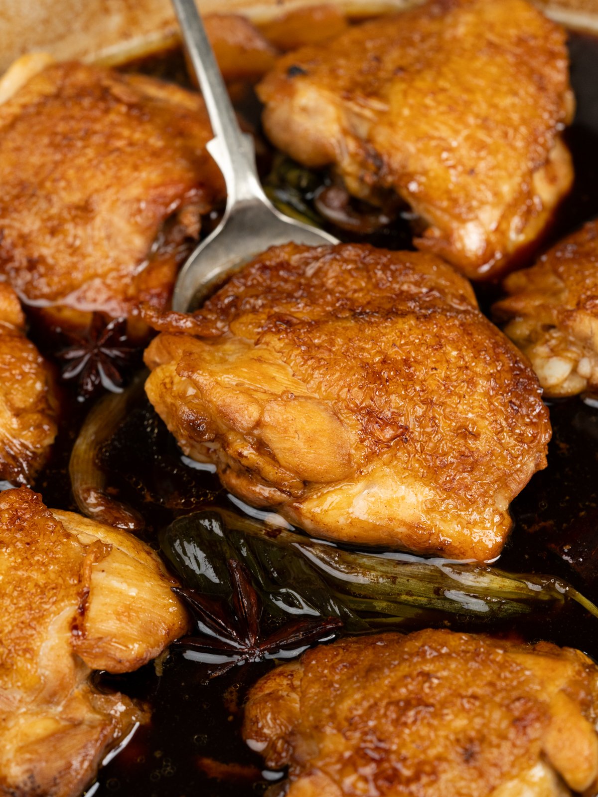 A spoon holding up a succulent piece of Soy sauce chicken.