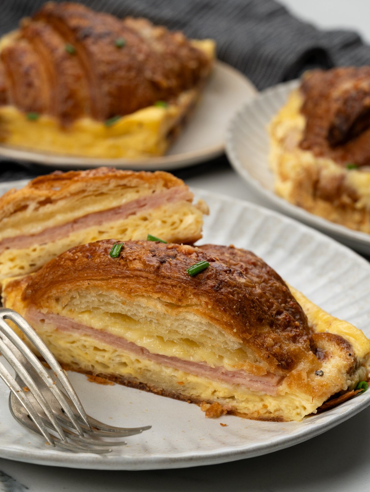 A large chunk of breakfast croissant casserole showing layers of ham and cheese in between.