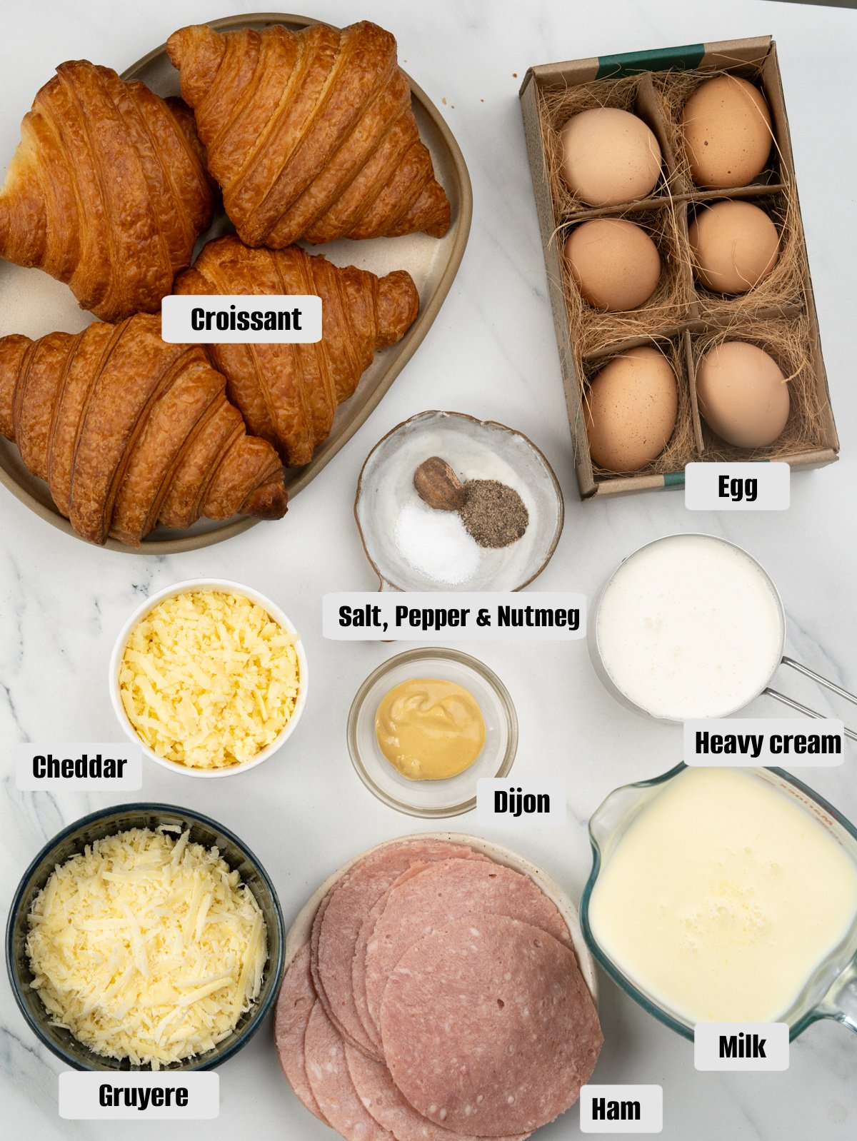 Ingredients for breakfast casserole - Croissants, Eggs, Milk, Heavy cream, Gruyere and Cheddar, Ham, Dijon mustard, salt, pepper and nutmeg.