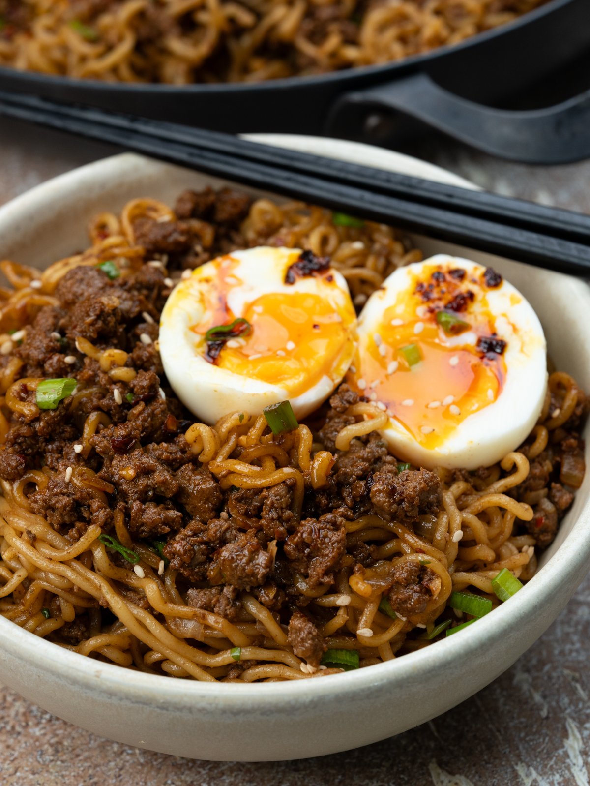 Bowl of Ground beef ramen noodles stir fry topped with jammy eggs, and drizzle of chilli crisp